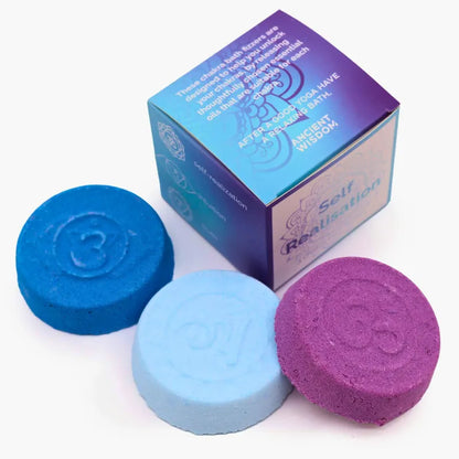 Trois bombes de bain chakra (violet, bleu foncé, bleu clair) avec détails gravés pour chaque chakra, accompagnées d’une boîte "Self Realisation" au design mandala. 